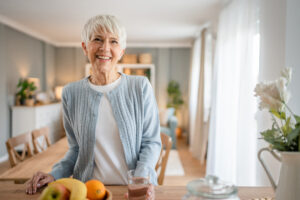 Close up portrait of one senior woman with short hair happy smile positive emotion copy space standing at home indoor gray white hair hold glass of water